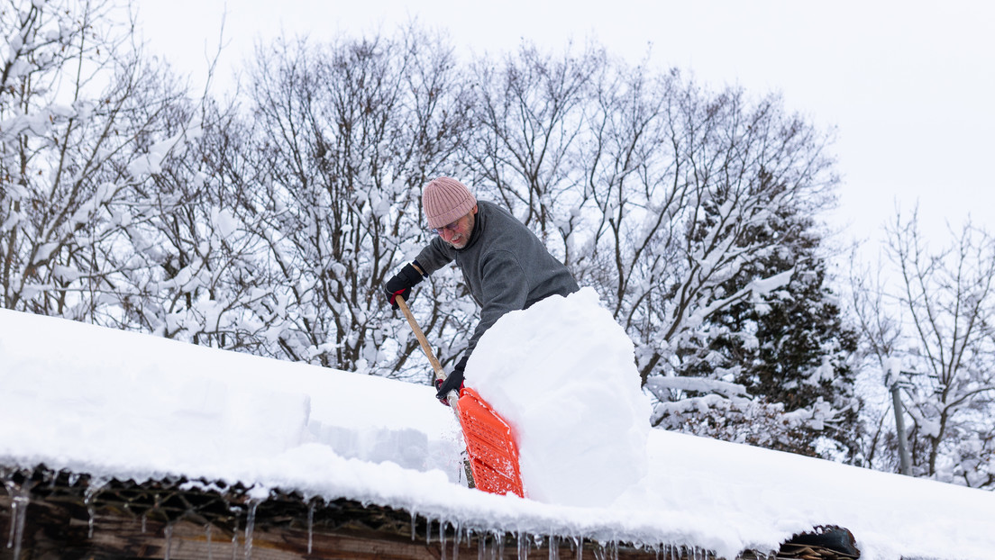Cómo un hombre limpia el techo del segundo piso cubierto de nieve